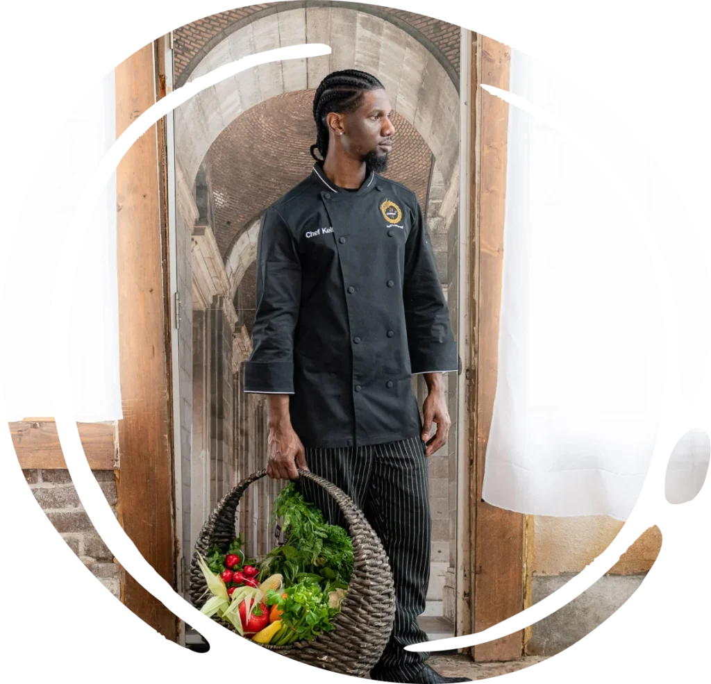A male chef in black uniform holds a basket of fresh produce