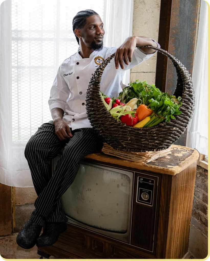 A chef keif sits on a vintage TV with a basket of fresh produce